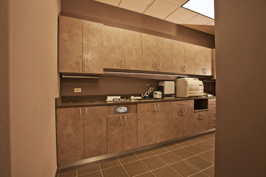 The image shows an interior view of a well-equipped office space with a focus on a counter area featuring cabinets, a sink, and various items typically found in such a setting.