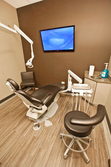 An interior view of a dental office with a modern chair, equipment, and a flat-screen television on the wall.