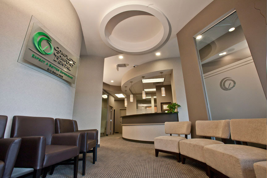 The image shows an interior space that appears to be a waiting area or lobby within a professional setting, featuring modern furnishings and decor, with a reception desk prominently displaying a sign.