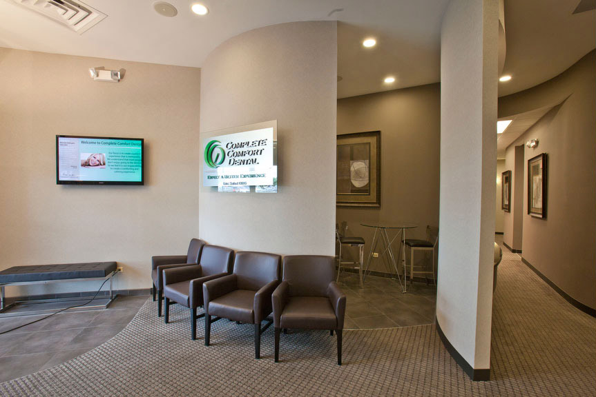 The image shows an interior space of a building, featuring a waiting area with seating, a television screen displaying information, and a sign with the text 'CQA' visible.