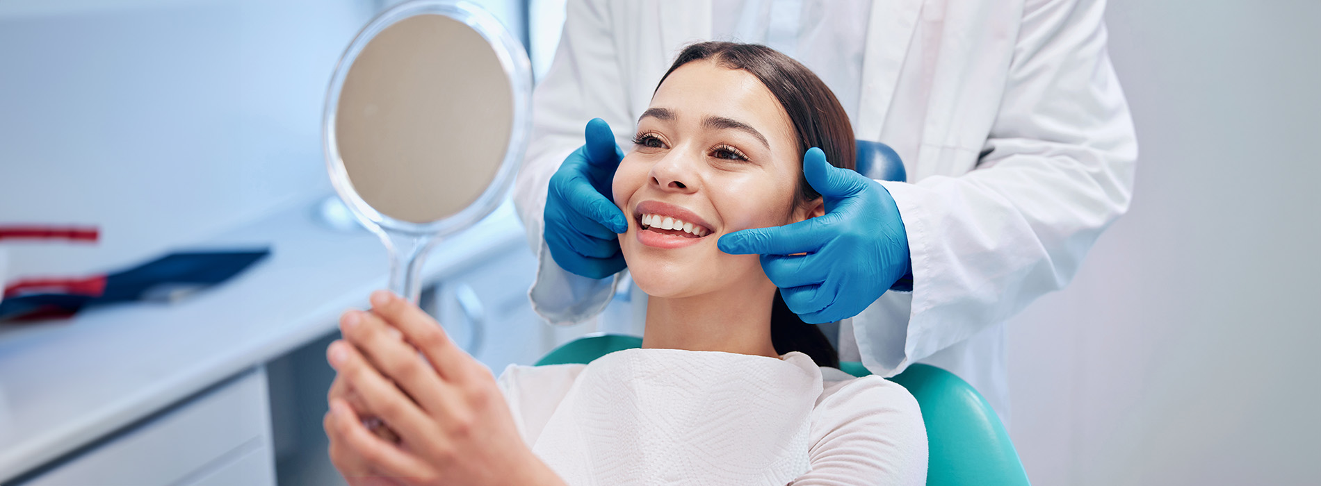 A woman in a dental chair receiving treatment from a dentist, with visible dental tools and equipment.