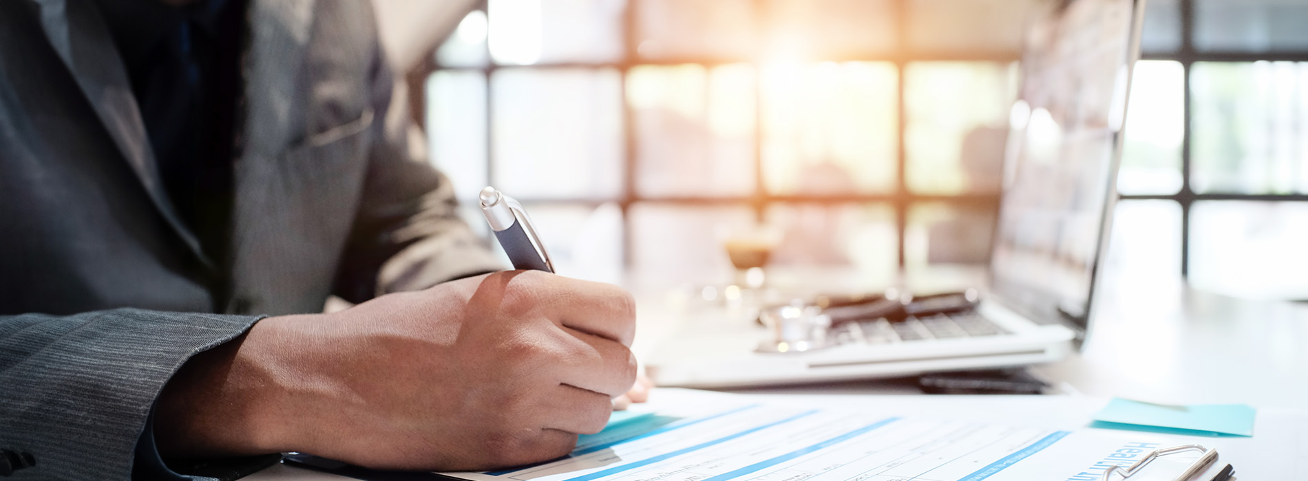 A person writing on a clipboard at a desk in an office environment.