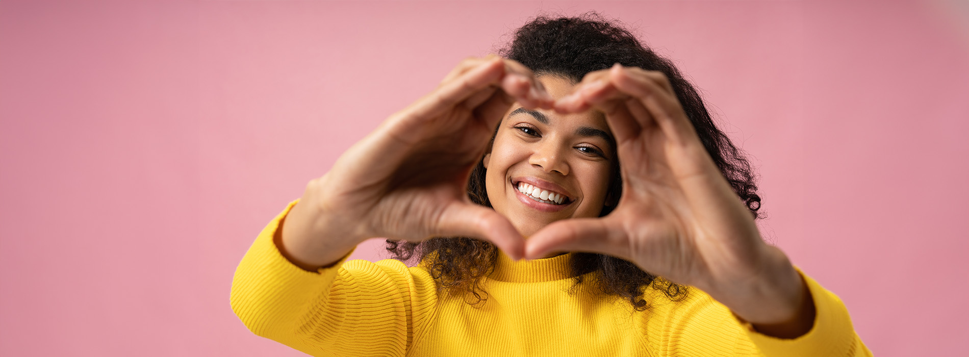 The image shows a person holding their hands together in the shape of a heart, with both hands visible and fingers spread apart to form the heart shape.