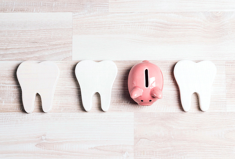Three tooth-shaped cutouts with a playful money pig in the center, placed on a light wooden surface.