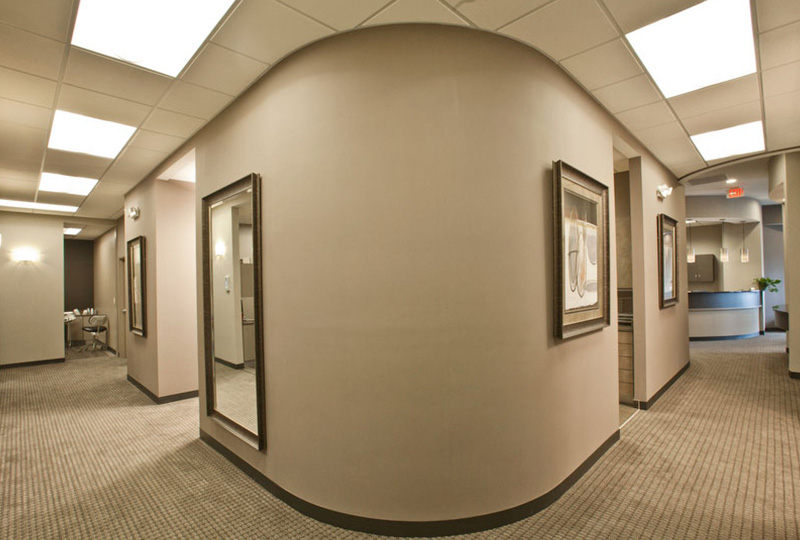 The image shows an interior space that appears to be a modern office or lobby with a curved wall, framed pictures on the wall, and a large circular mirror at the end of the hallway.