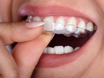 An image of a person holding a toothbrush with toothpaste and looking at it closely, set against a blurred background.