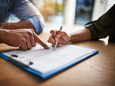 Two individuals signing a document on a table with a clipboard and pen.