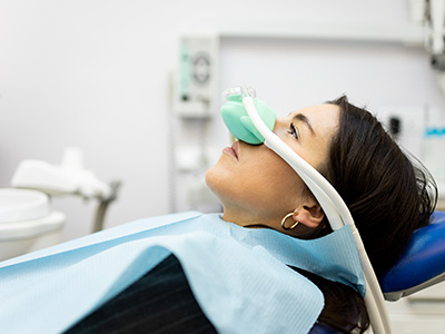 An individual wearing a medical mask is seated in a dental chair, receiving treatment.