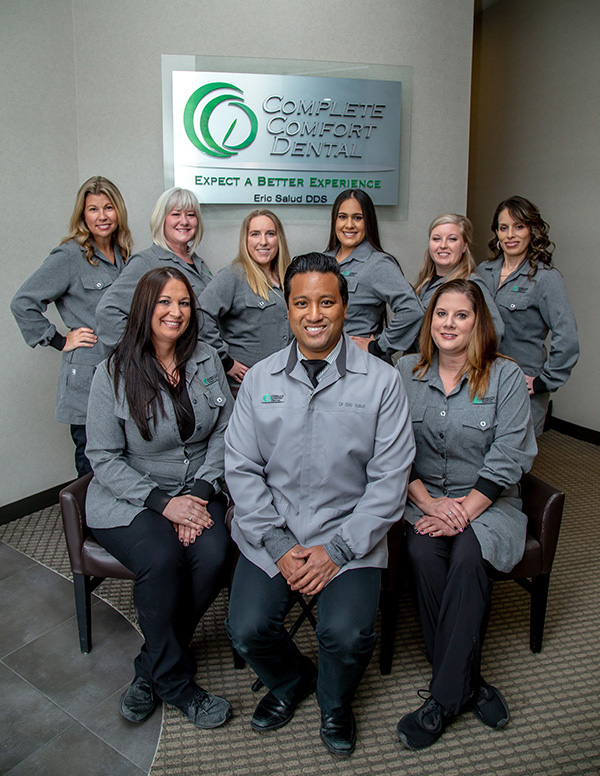 A group of individuals, likely dental professionals, posing for a photo in front of a sign that reads  Complete Dental Services  and  Expect a better experience.