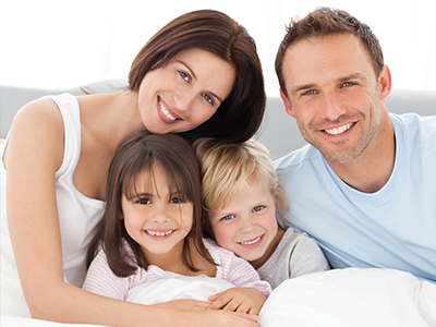 The image shows a family of four, including an adult couple and their two children, posing for a photo in bed.